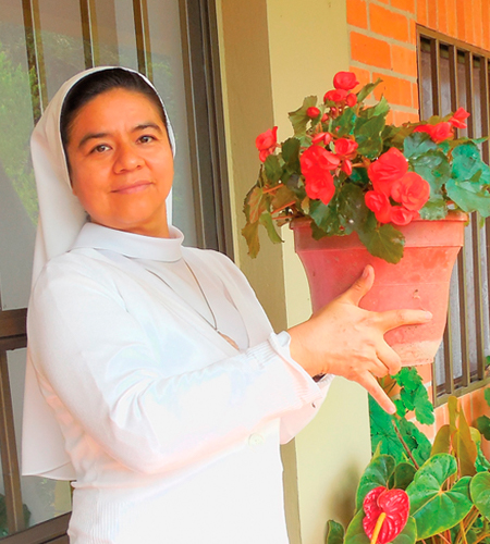 Photographie d'une soeur Oblates de Béthanie colombienne tenant un pot de fleurs rouges.