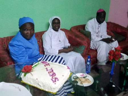 Dans la nouvelle Maison des Oblates de Béthanie au Burkina Faso, en Afrique, quelques soeurs assises et partageant le dessert avec Mgr Lucas Sanou.