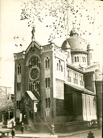Photographie d'époque montrant la chapelle Notre-Dame-de-Lourdes à Montréal et devant laquelle défilent quelques passants